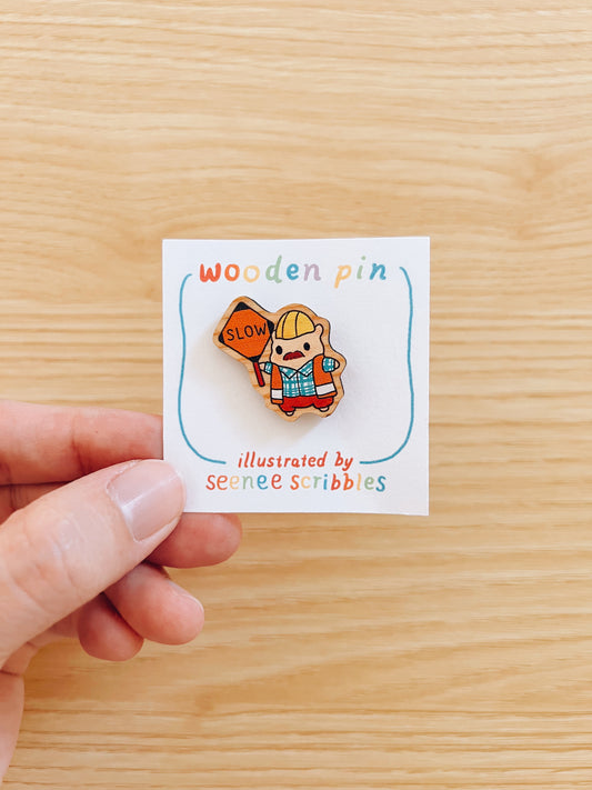 Hand holding a wooden pin with a construction worker hamster design on a white card with text.